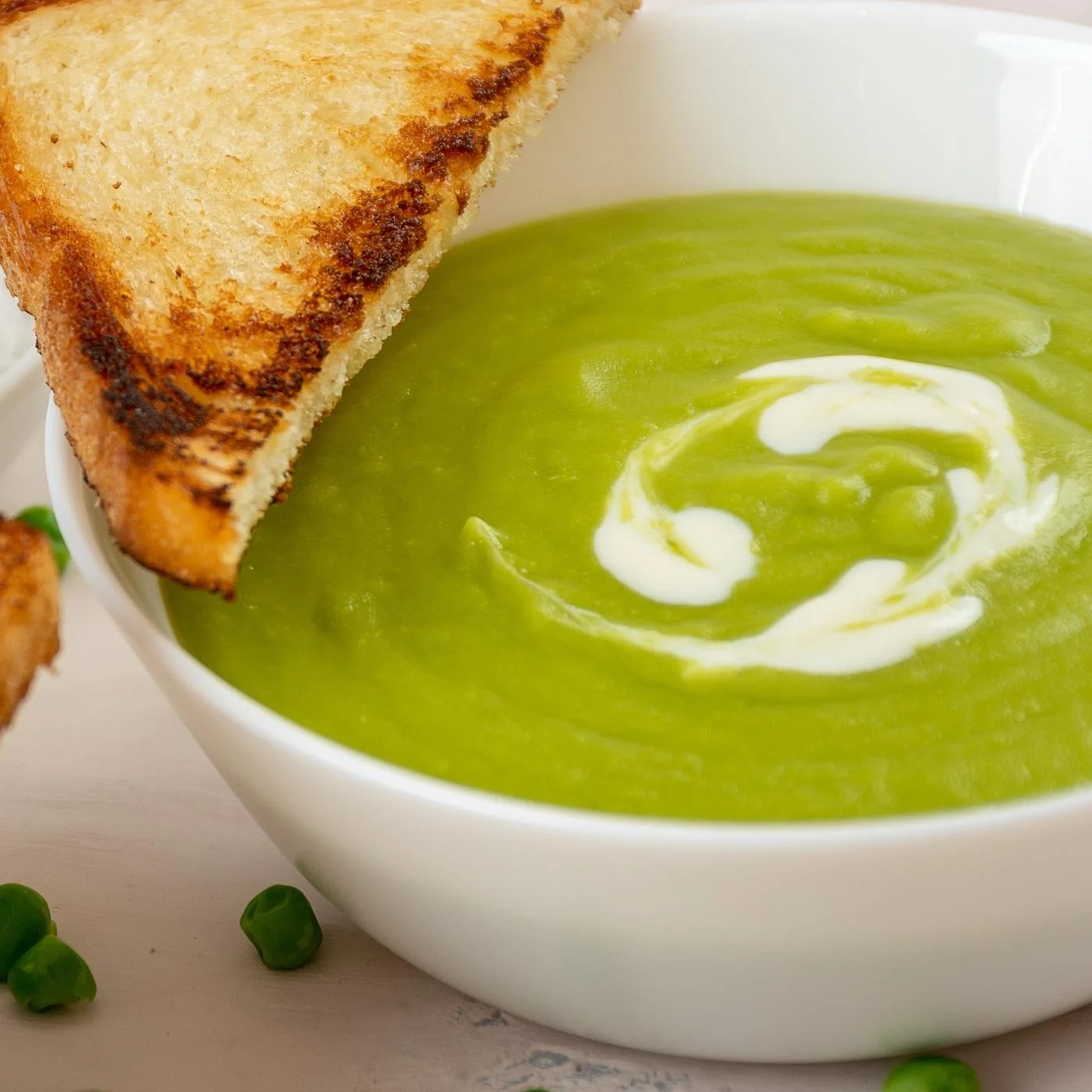 Light green pea soup in a bowl, with a touch of sour cream, and nice piece.