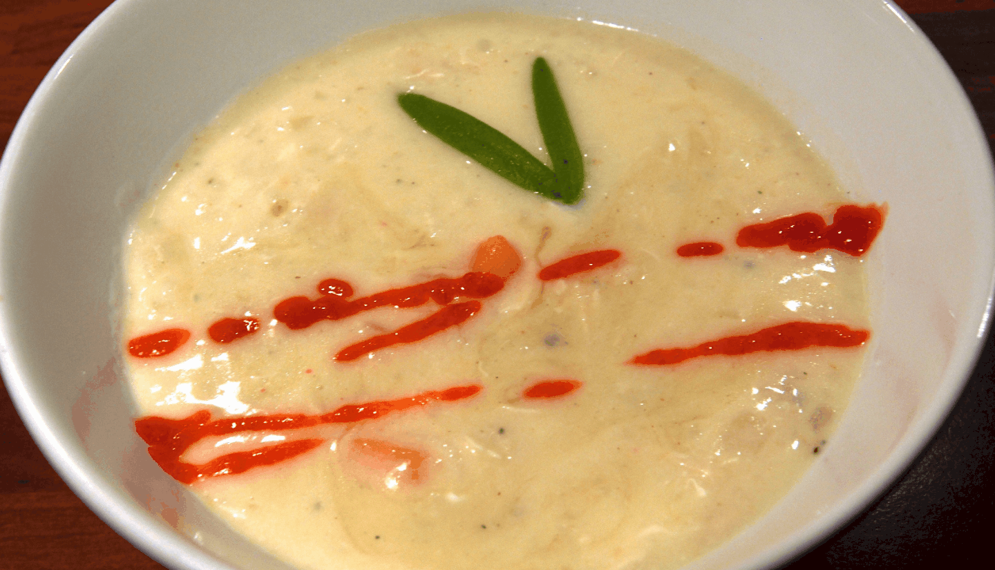 Greek lemon chicken soup serve in a white plate with a red sauce and herb on top