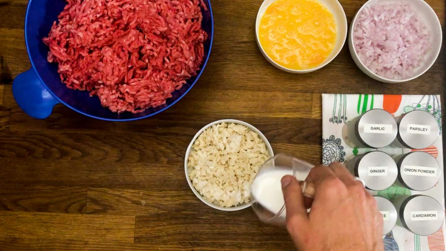 ground beef in blue mixing bowl, egg, onion, and bread crumbs