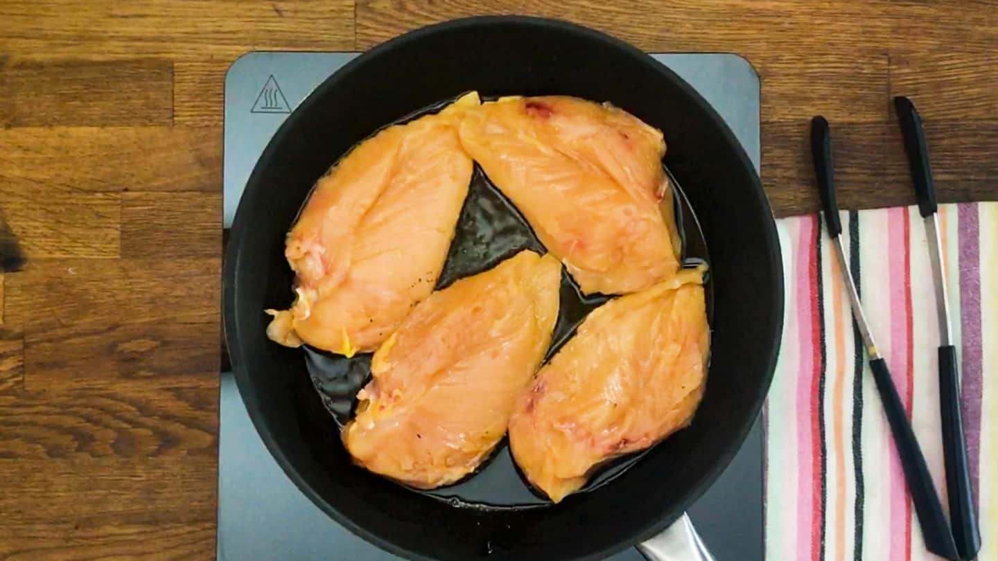 Four chicken breast cooking in cast iron skillet