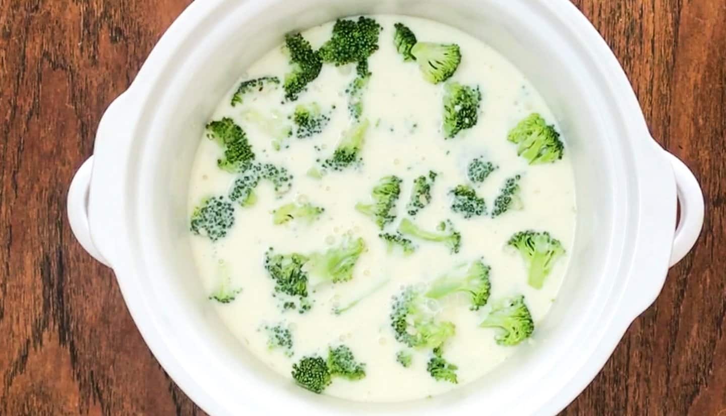 a slow cooker pot with broccoli and cream milk mixture