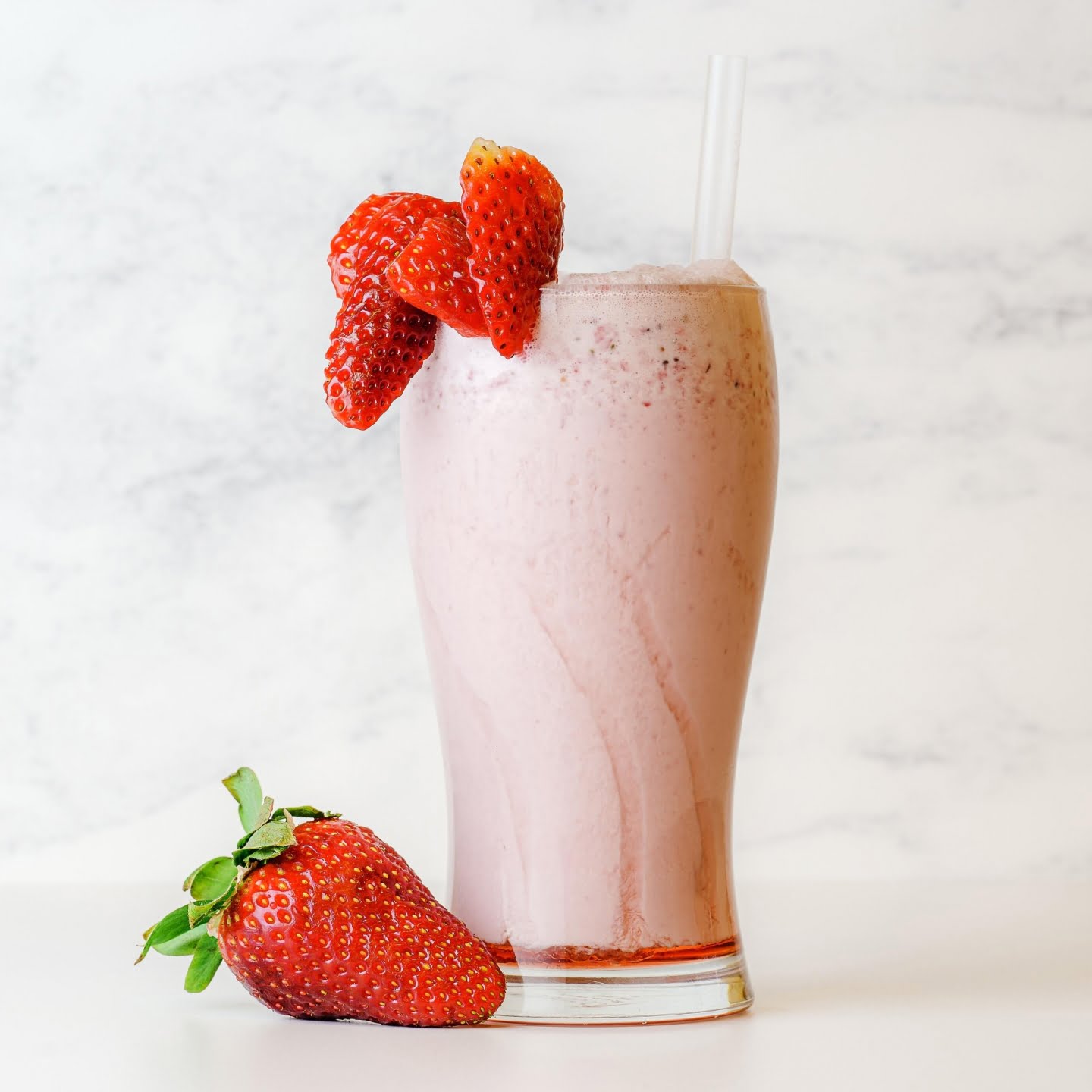 Strawberry milkshake in a tall glass with fresh strawberries on the side