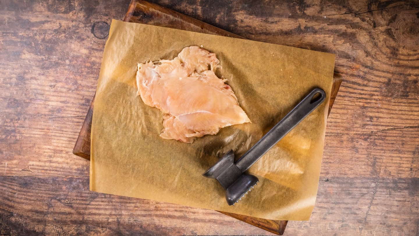 Chicken breasts on a chopping board using a meat tenderizer