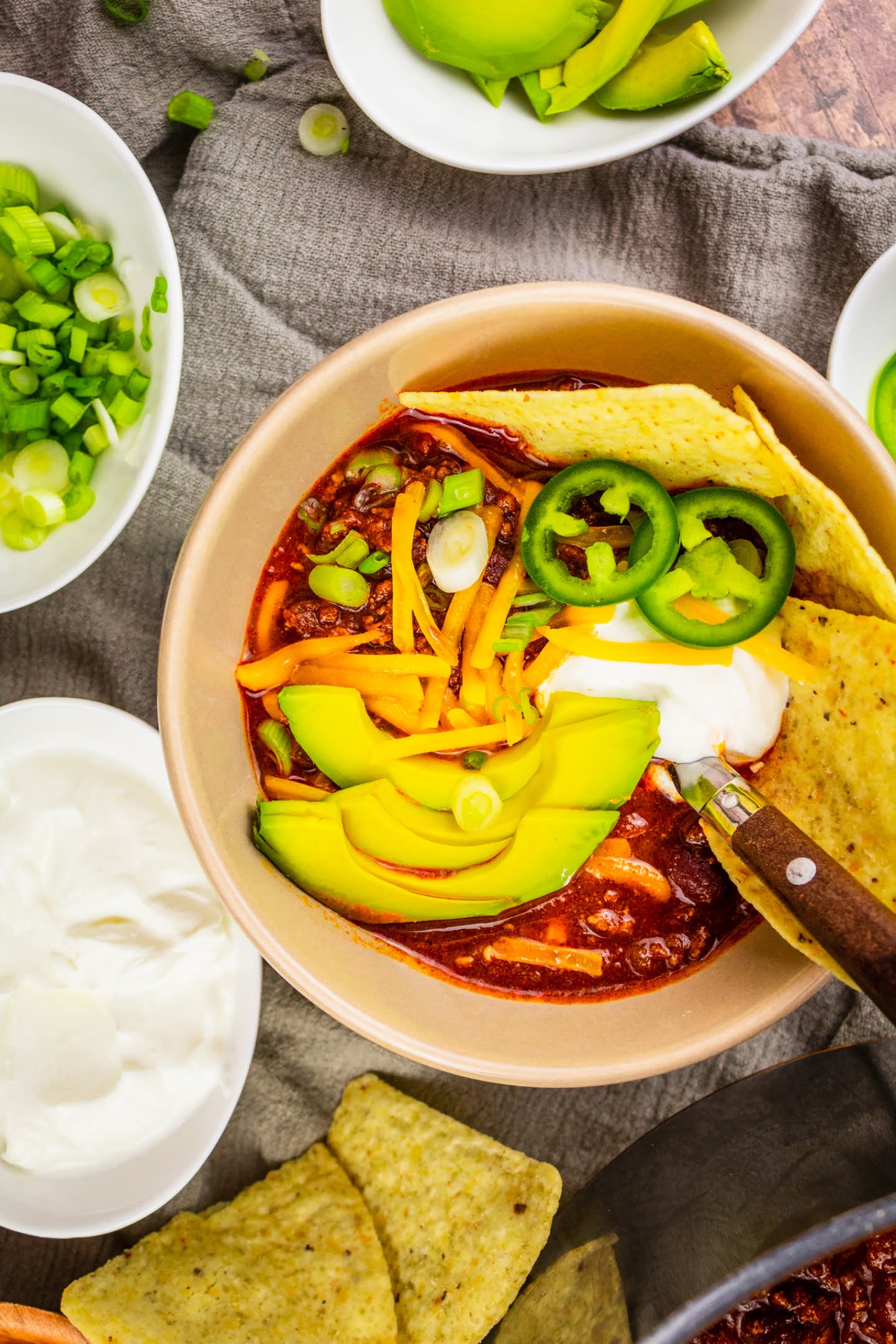 Chili in a bowl with topping avocado tortilla chips cheese jalapenos sour cream