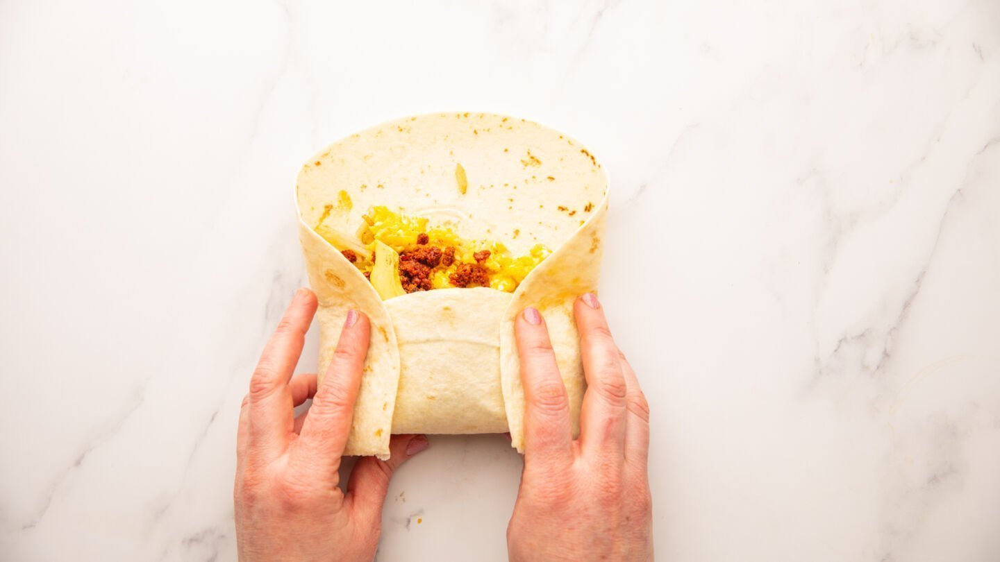 Using both hands, fold the edges of the warm tortilla in and roll the bottom of the tortilla over the filling and tuck the tortilla under it, rolling the tortilla to complete the burrito.