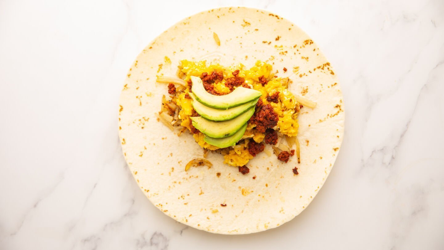 To assemble the burritos, evenly divide the cooked chorizo, cheesy scrambled eggs, and cooked potatoes across the middle of the warm tortillas, then top with the sliced avocado
