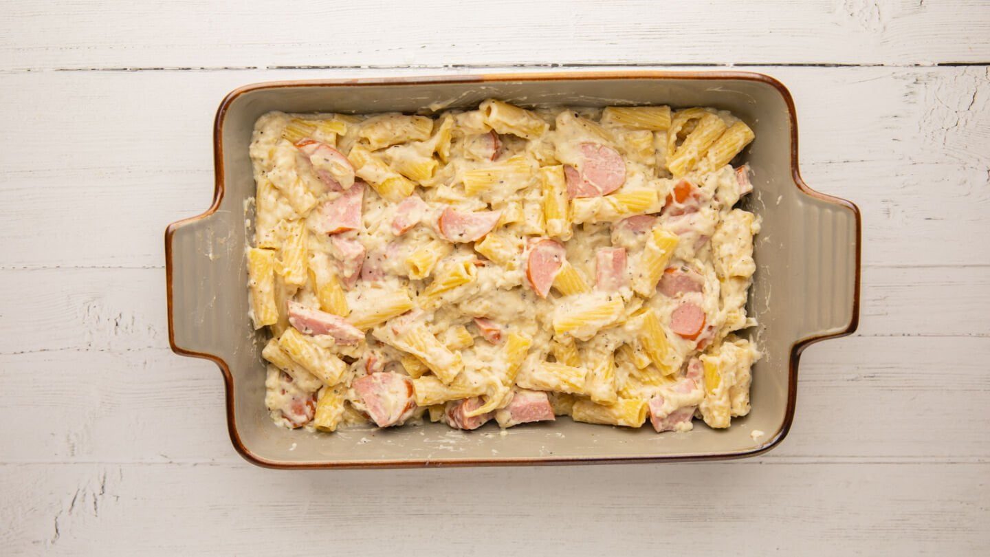 Pour the cooked pasta, creamy sauce, and sliced sausage into the baking dish