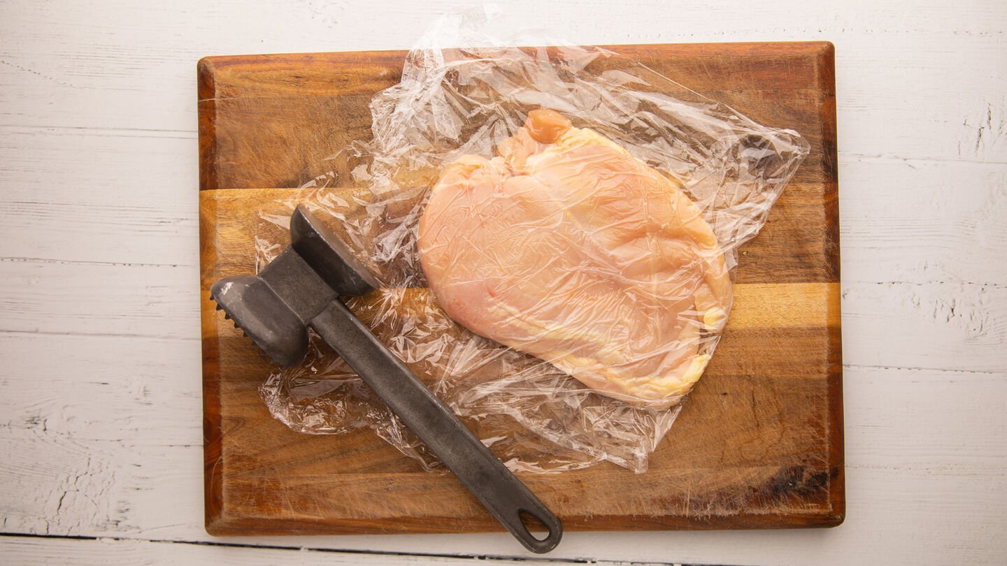 place a layer of plastic wrap on a cutting board and a chicken breast on top.