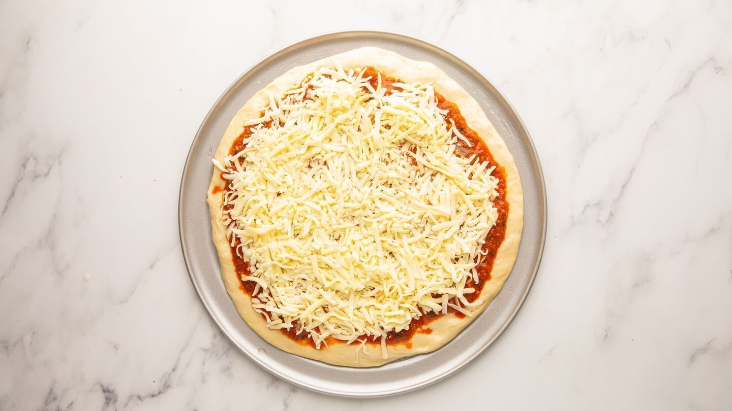 Top with fresh mozzarella cheese, followed by the remaining Greek pizza ingredients.