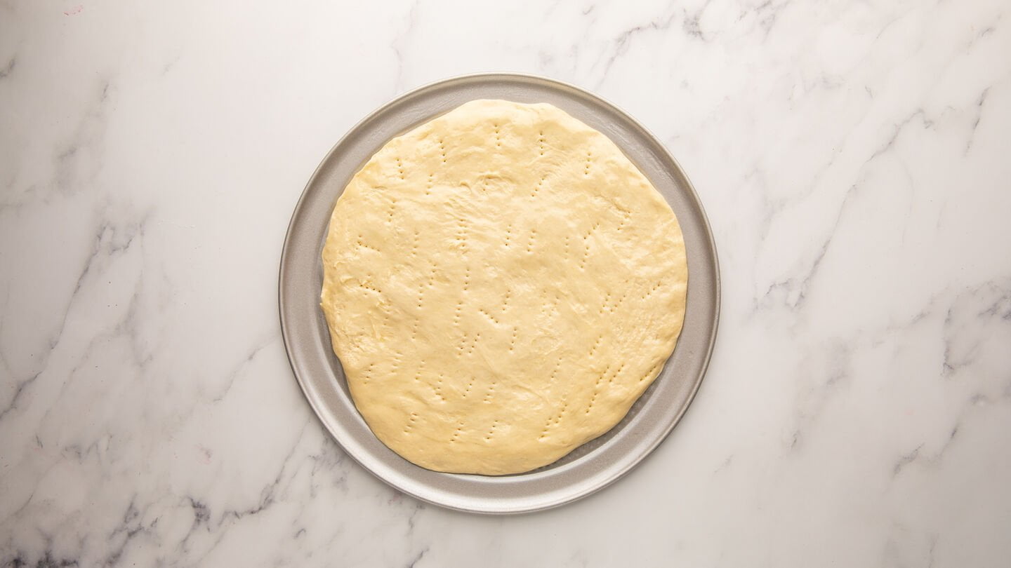 Transfer the pizza dough to your prepared pizza pan and lightly brush the edges with olive oil